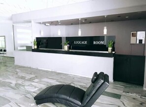 Un mostrador de recepción con cartel que indica 'LUGGAGE ROOM', una silla de cuero negro y suelo de mármol.