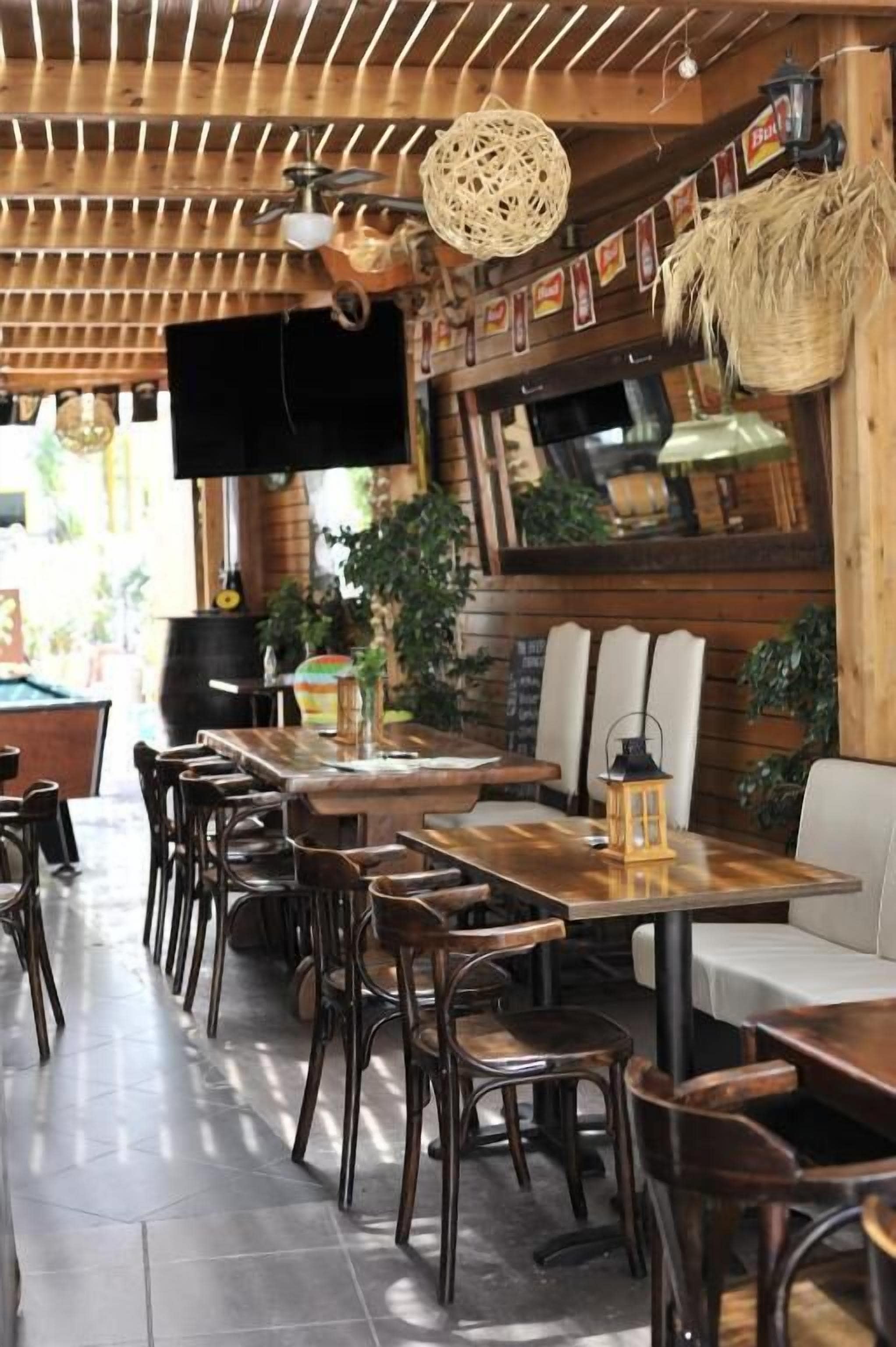 Un restaurant avec des tables et des chaises en bois, un téléviseur fixé au mur et diverses décorations, notamment des plantes et des lanternes.
