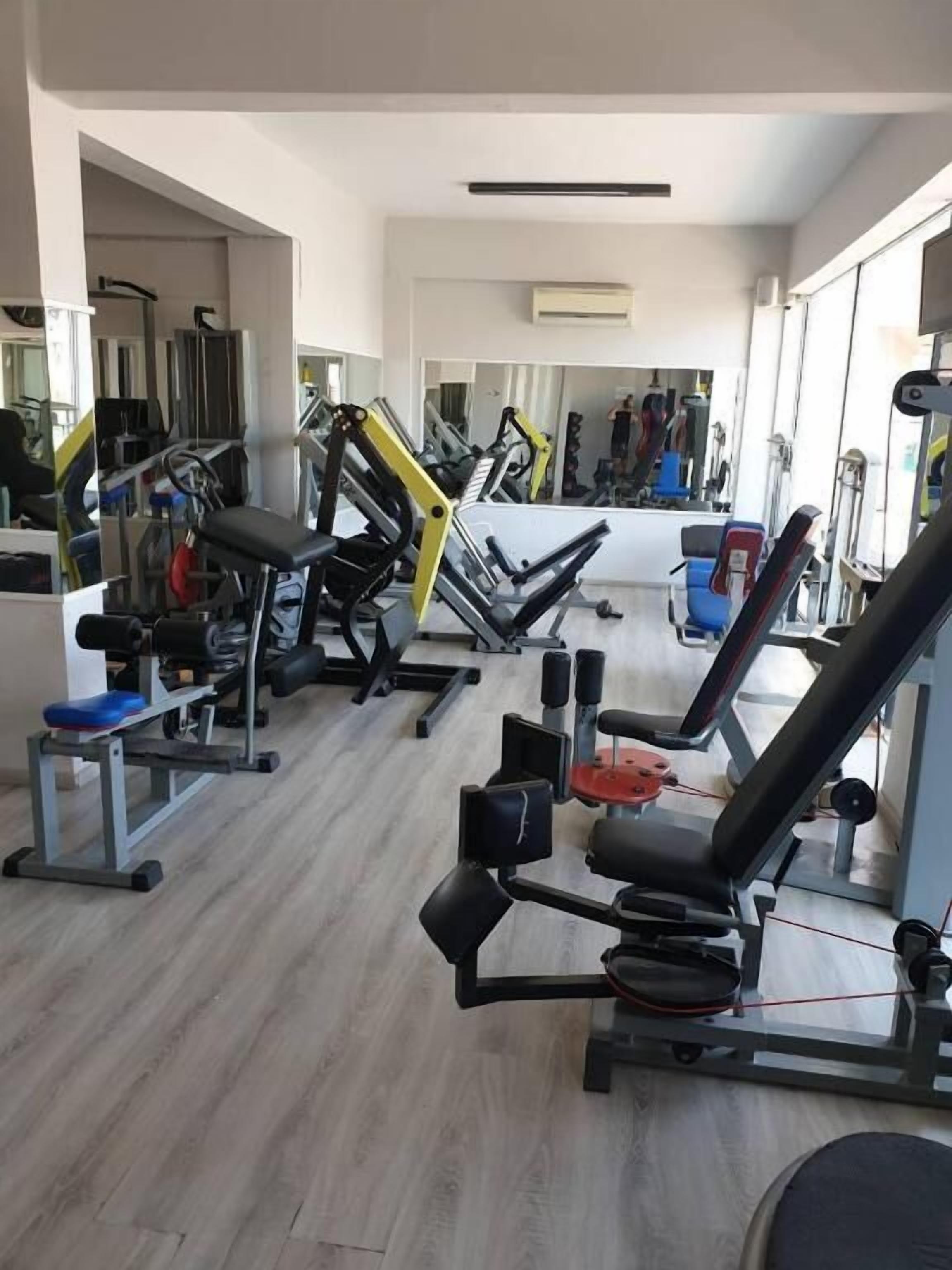 A gym with various exercise machines, a mirror, and a window providing natural light.