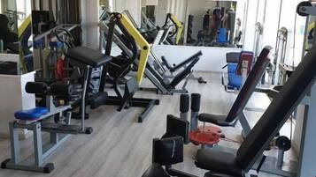 A gym with various exercise machines, a mirror, and a window providing natural light.