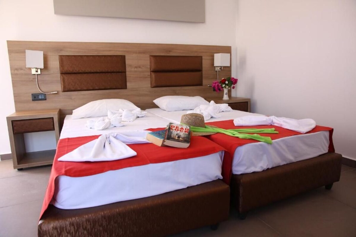 Habitación de hotel con dos camas, cabecero de madera, mesitas de noche y una lámpara de pared.