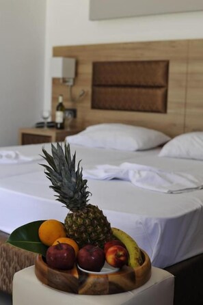 Een bed met houten hoofdeinde, een nachtkastje met een fles en een fruitschaal op het nachtkastje.