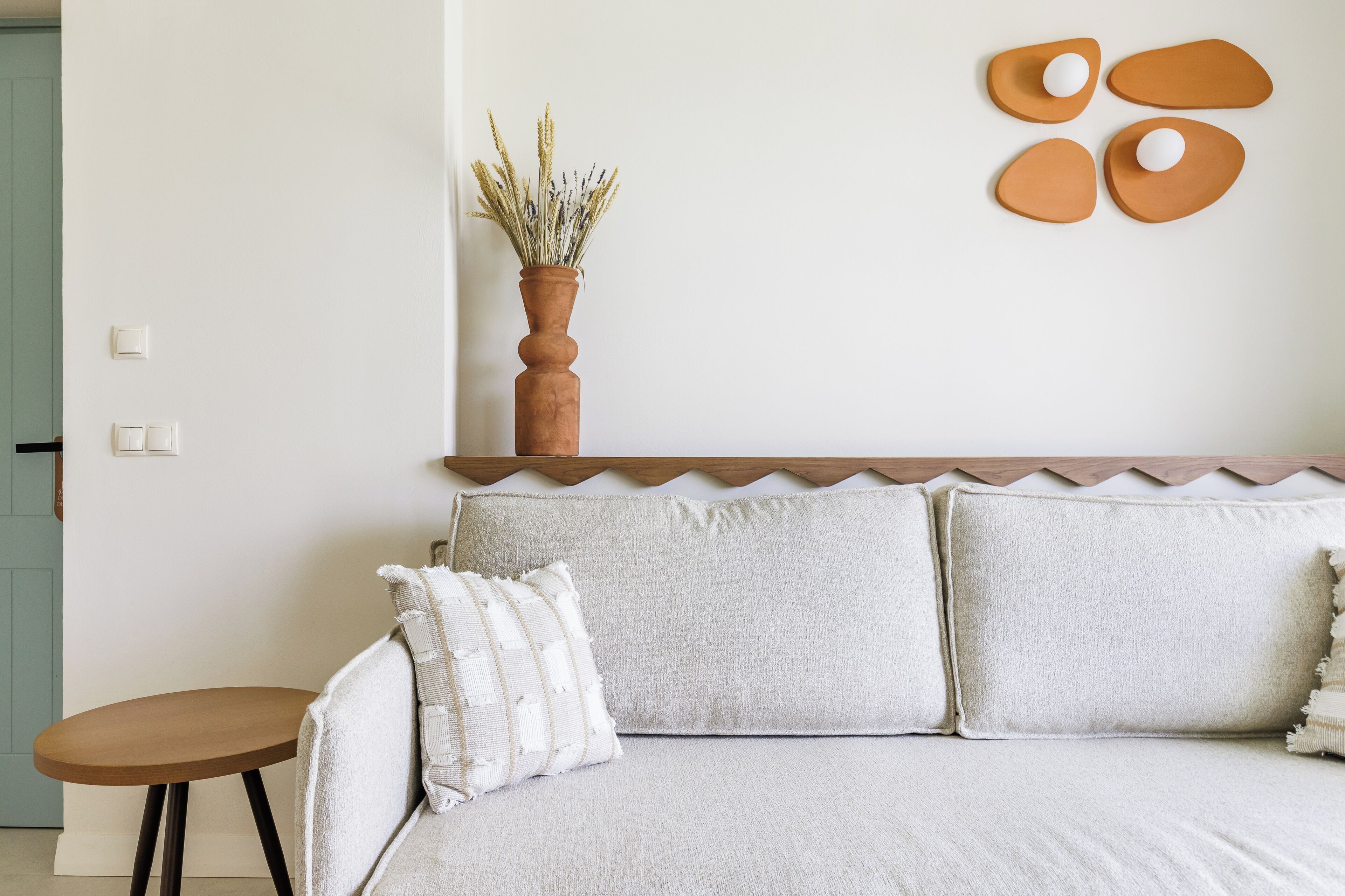 A bedroom with a bed, a small table, and a wall-mounted shelf with a vase of dried plants.
