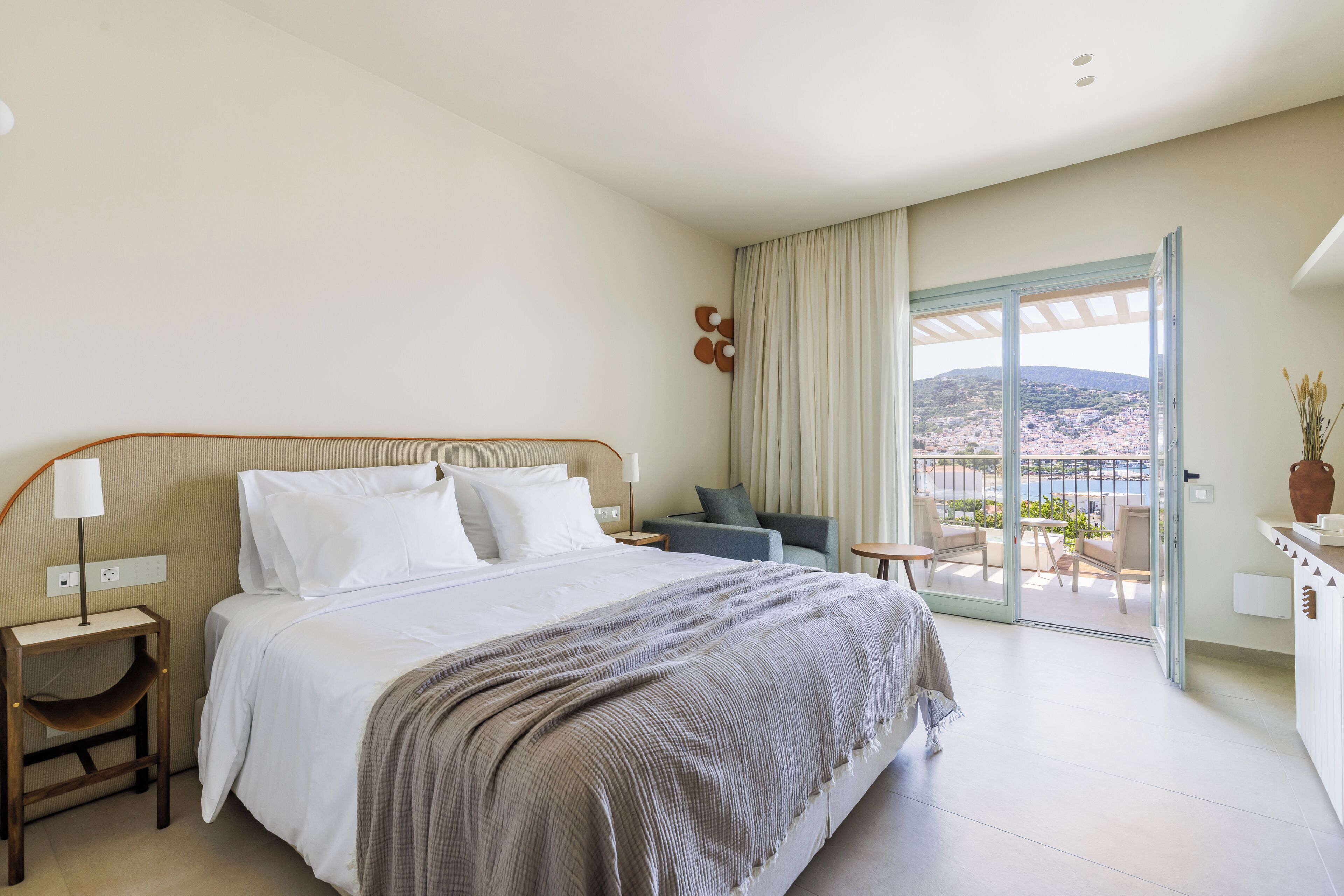 A hotel room with a bed, a seating area with a view, and a balcony with a cityscape view.