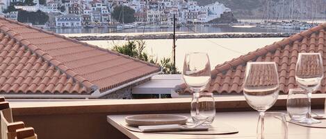 A dining table set for two with a view of a coastal town and hills in the background.