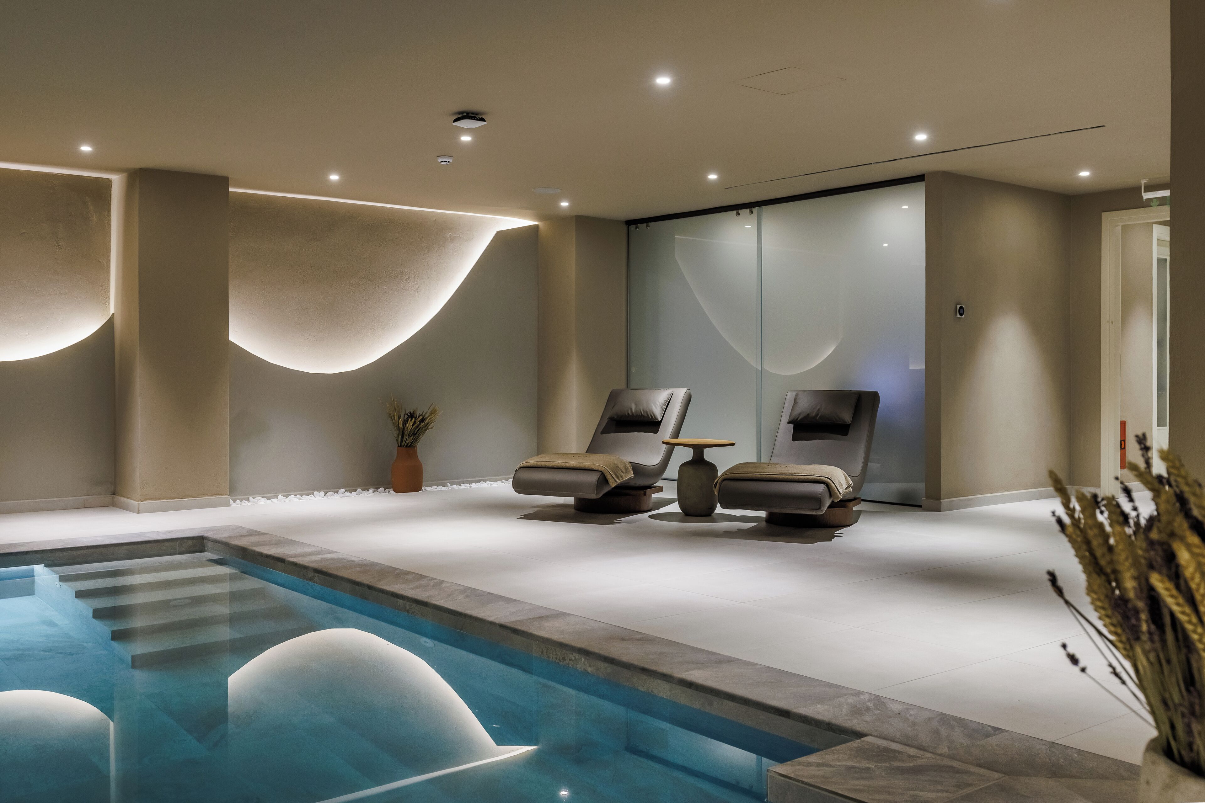 Uma área de spa moderna com piscina, duas espreguiçadeiras e uma mesa de massagem.