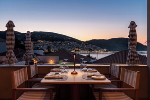 A dining table set for six with striped umbrellas and a view of a town and hills in the background. - Minnŏ Boutique Hotel & Spa (Skopelos)