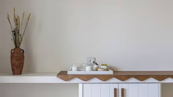 Ein weißes Regal mit Holzbeschichtung, eine braune Vase mit Trockenpflanzen und eine Ablage mit weißen Tassen und Schalen.