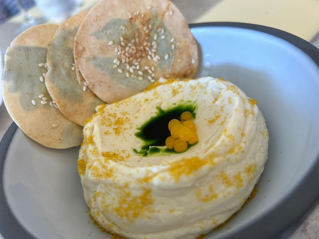 A plate with a white, round food item topped with yellow seeds, accompanied by two flatbreads with sesame seeds.