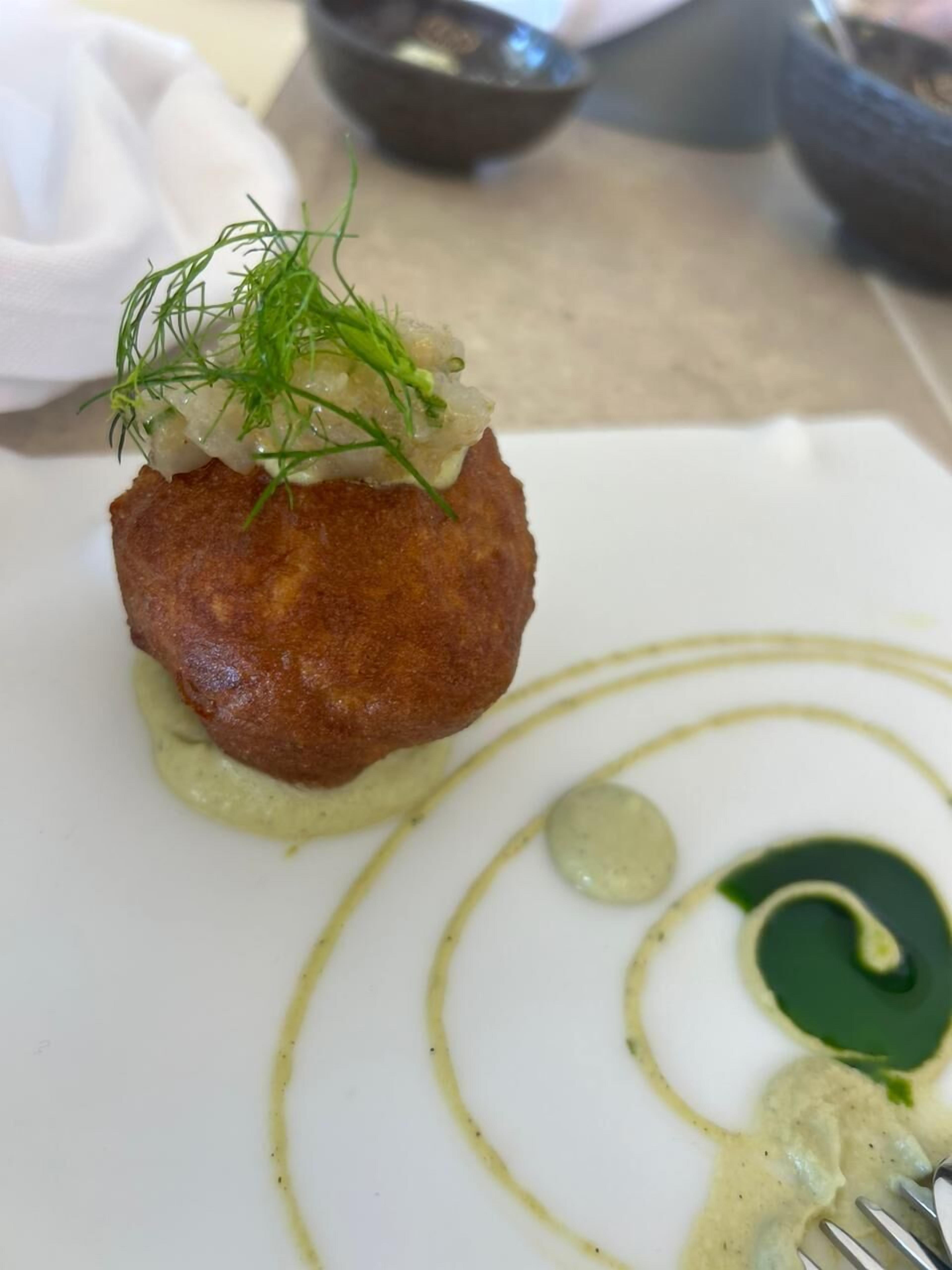 A plated dish with a golden-brown item, a green sauce, and a garnish on a white plate.