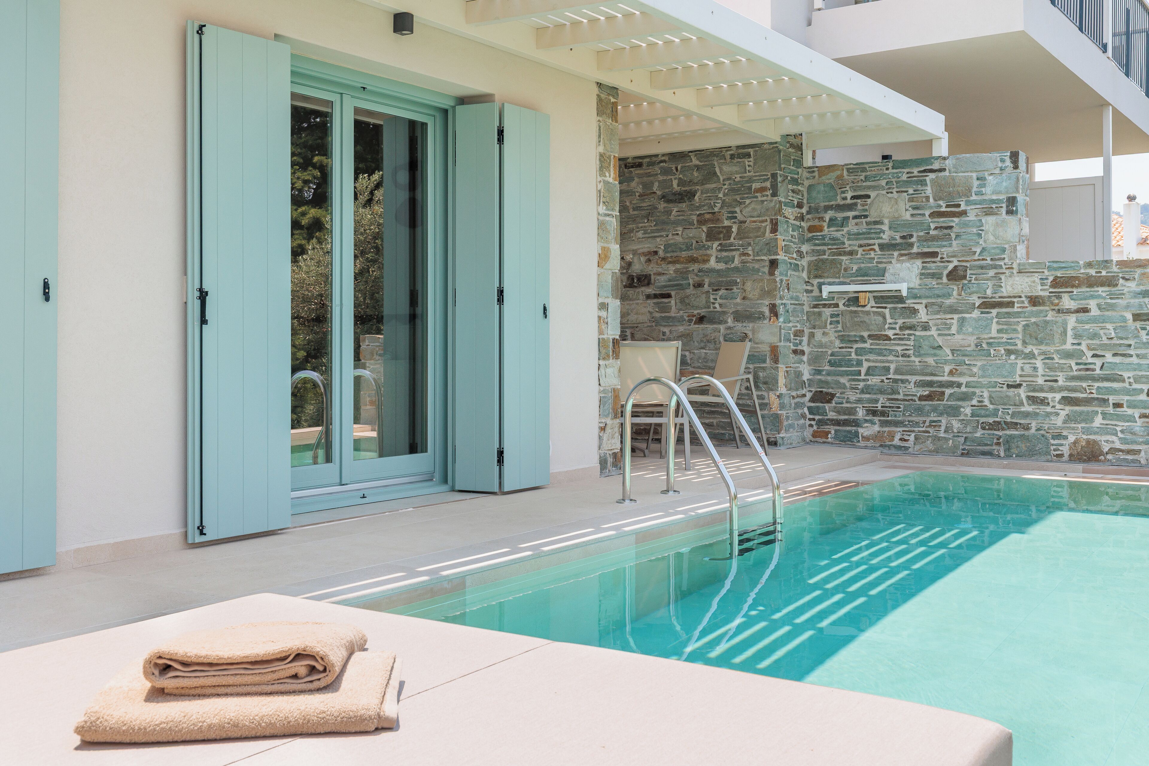 A modern pool area with a stone wall, a chair, and a towel on a lounge chair.