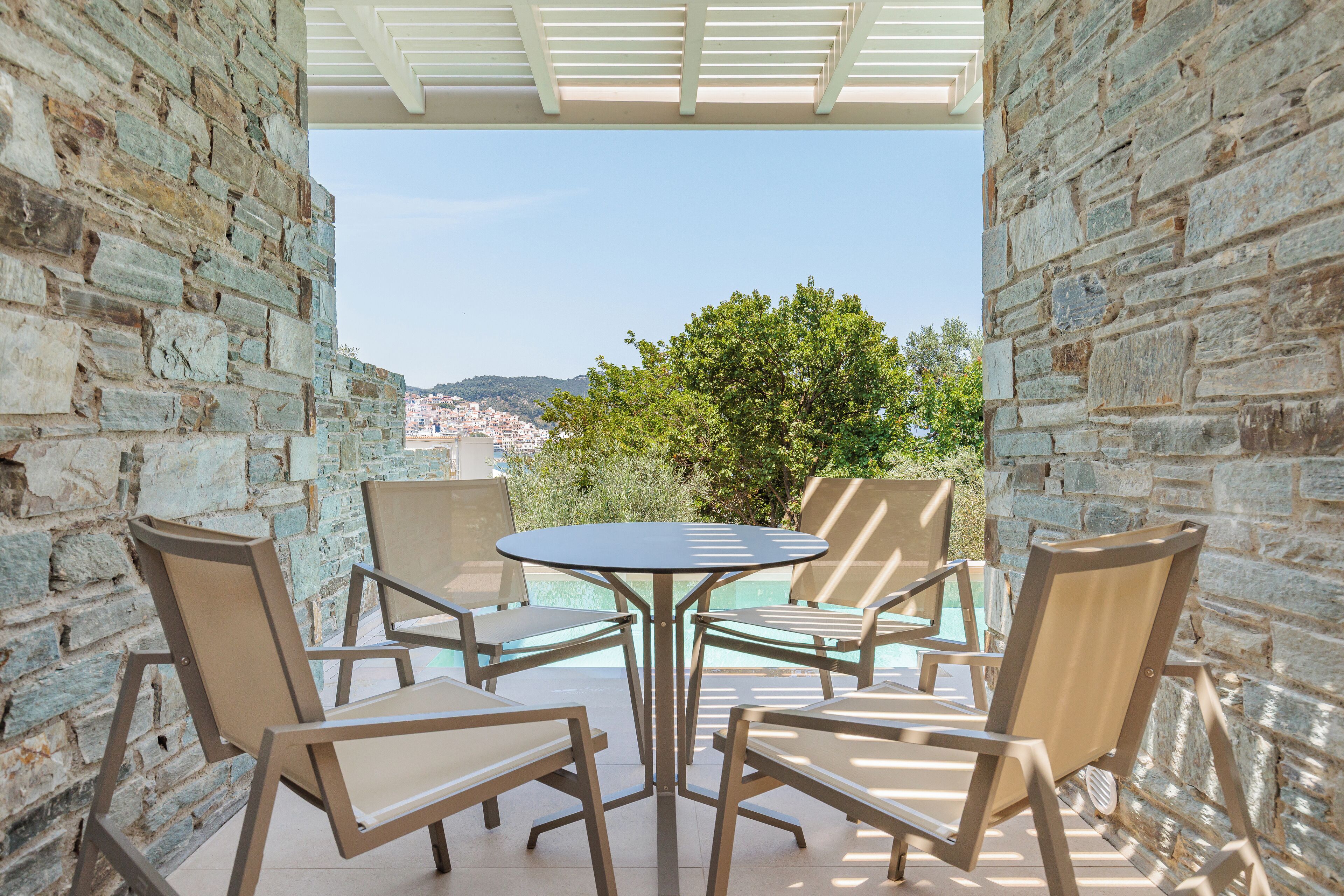 A stone-walled outdoor seating area with a round table and four chairs, overlooking a scenic landscape.