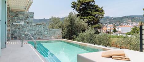 A modern outdoor pool area with stone walls, a metal railing, and a view of a town in the background.