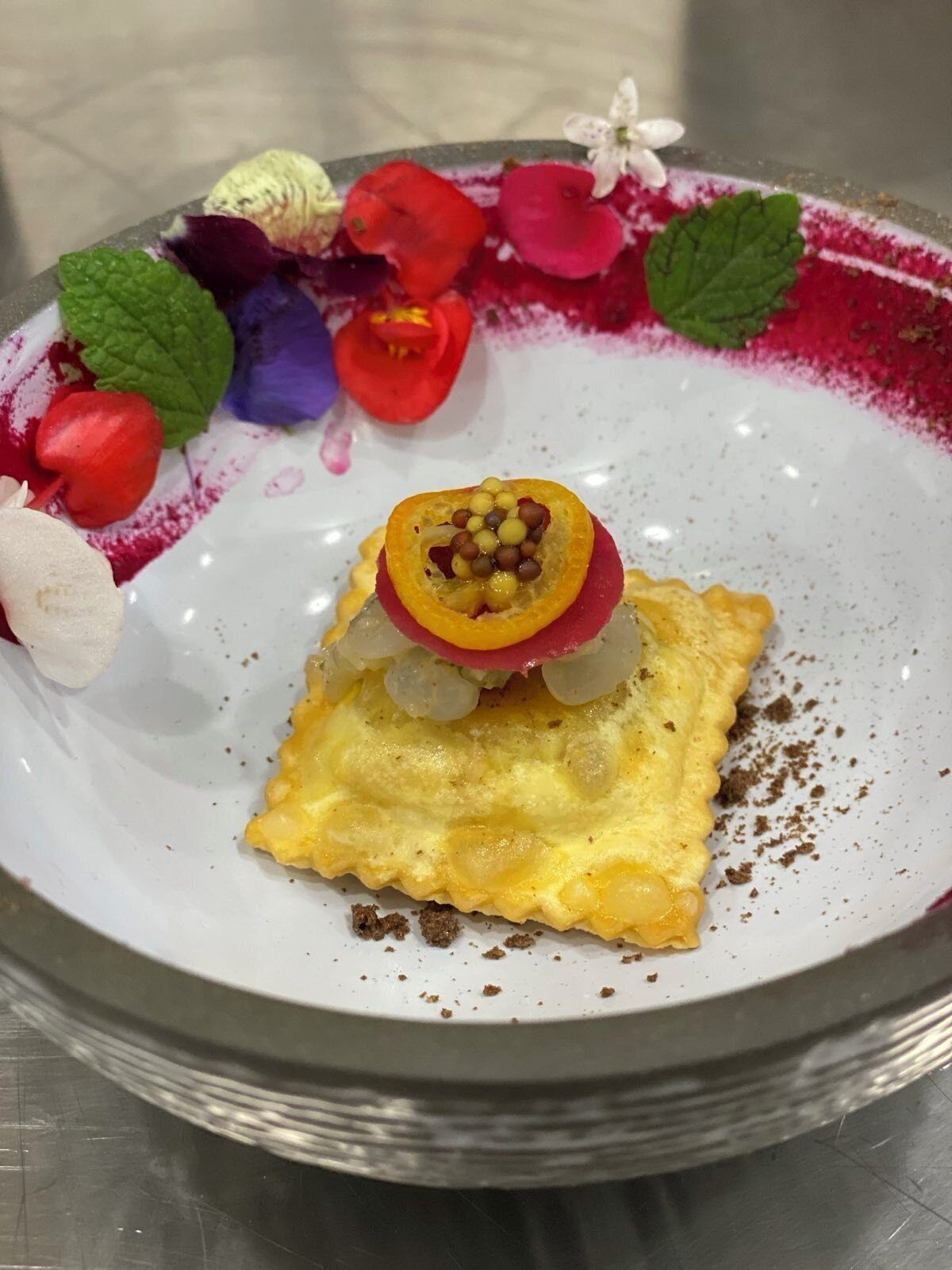 A dessert plate with a square pastry, garnished with a slice of fruit and a decorative flower.