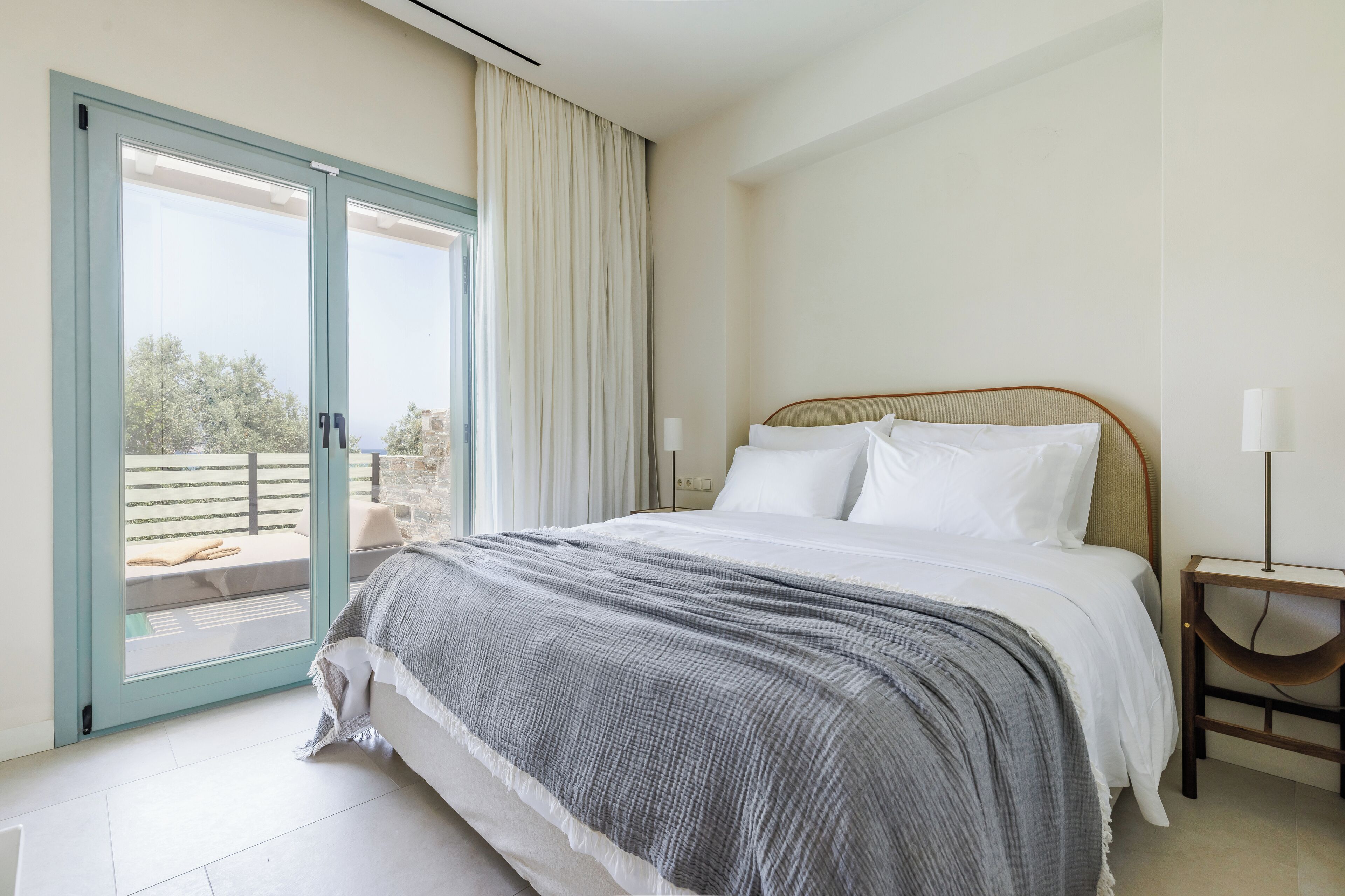A bedroom with a bed, a nightstand, a lamp, a sliding glass door, and a view of the outdoors.