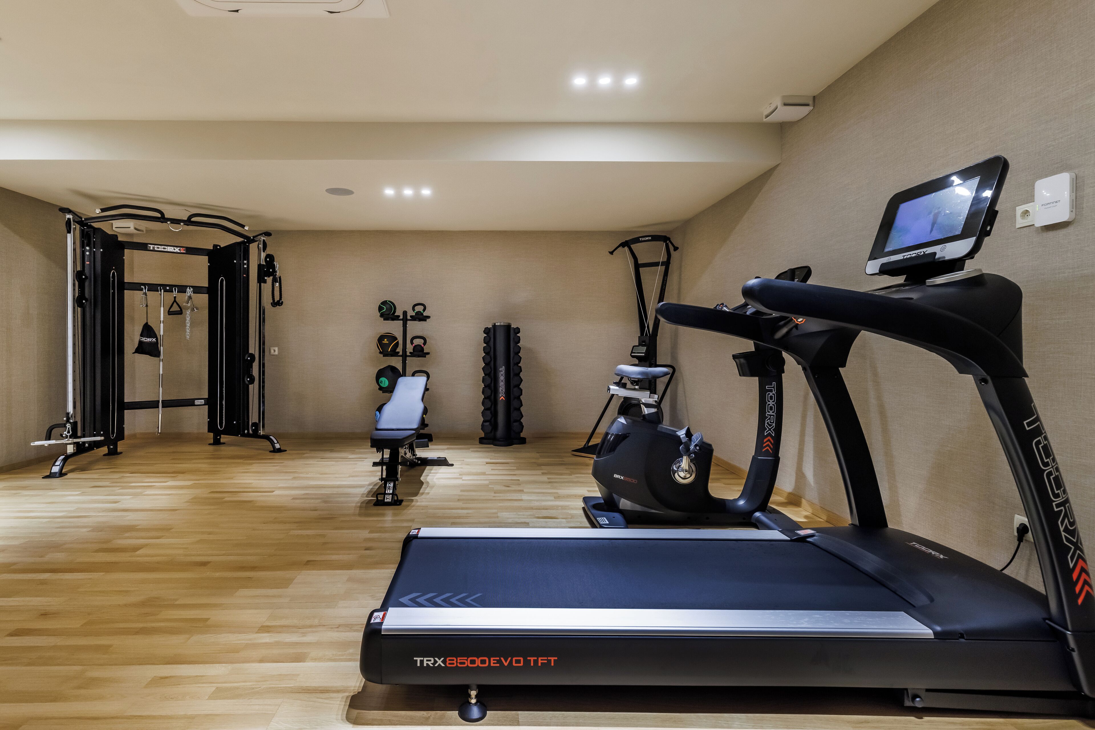 A gym with a TRX 8500 EVO TPT treadmill, a pull-up bar, a bench, and a stationary bike.