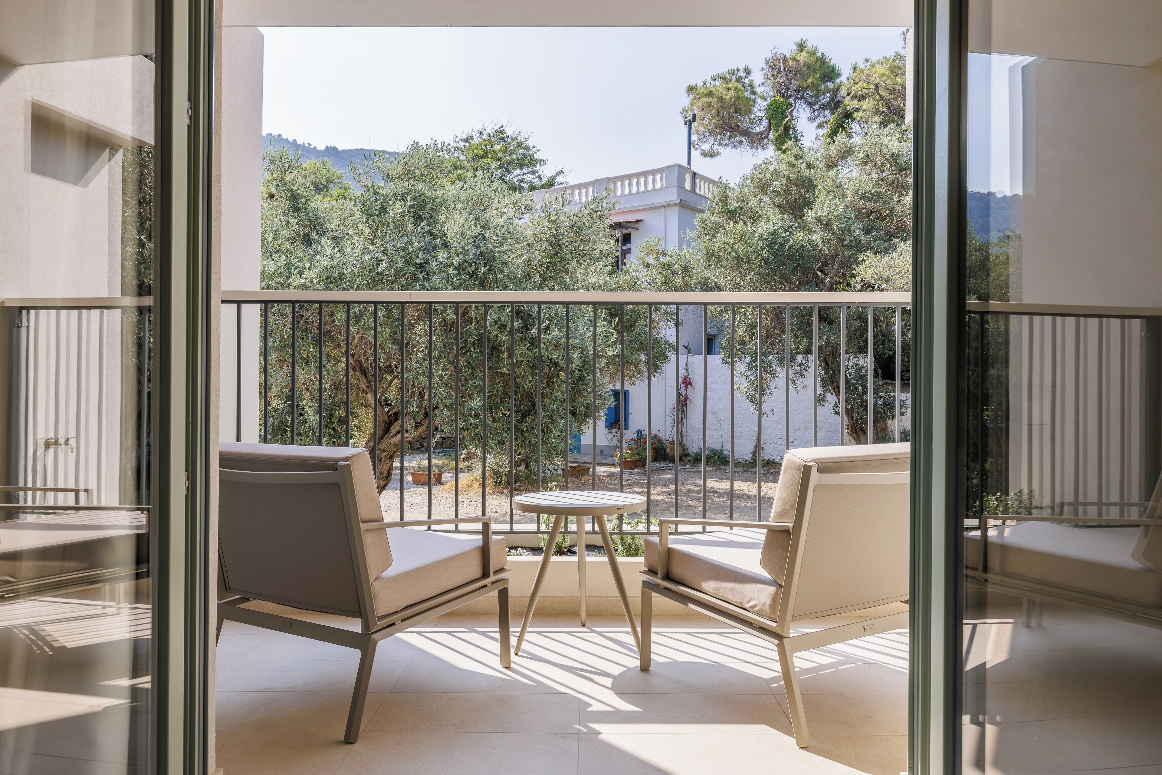 A balcony with two chairs and a small table, offering a view of a building and trees.