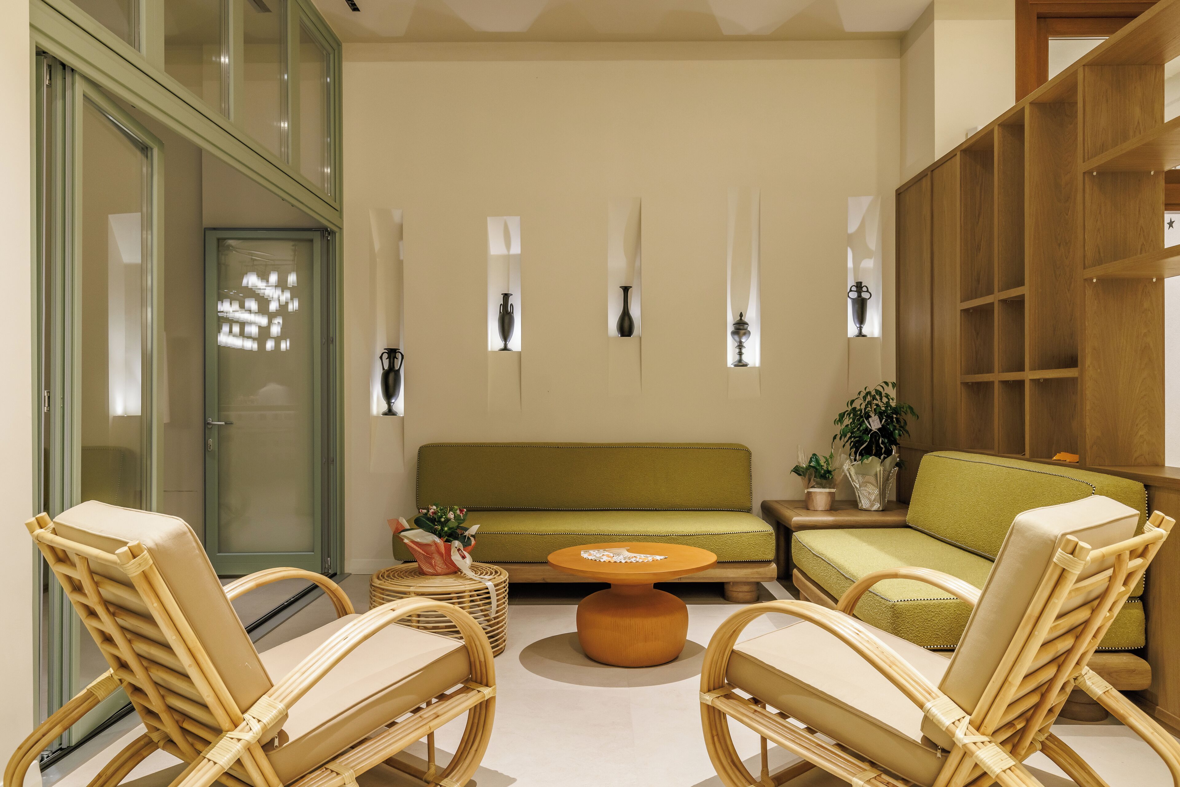 A modern living room with a green sofa, wicker chairs, a round coffee table, and a wooden bookshelf.