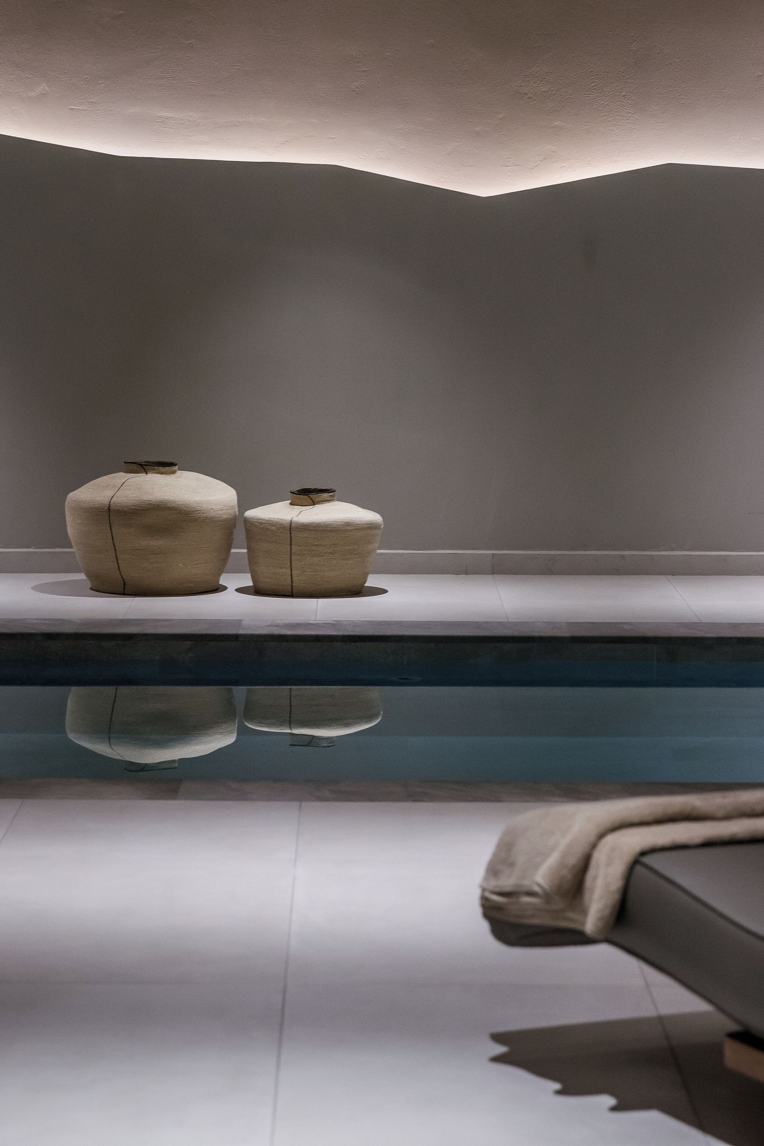 A minimalist bathroom with a large mirror, a bathtub, and two ceramic vases on a shelf.