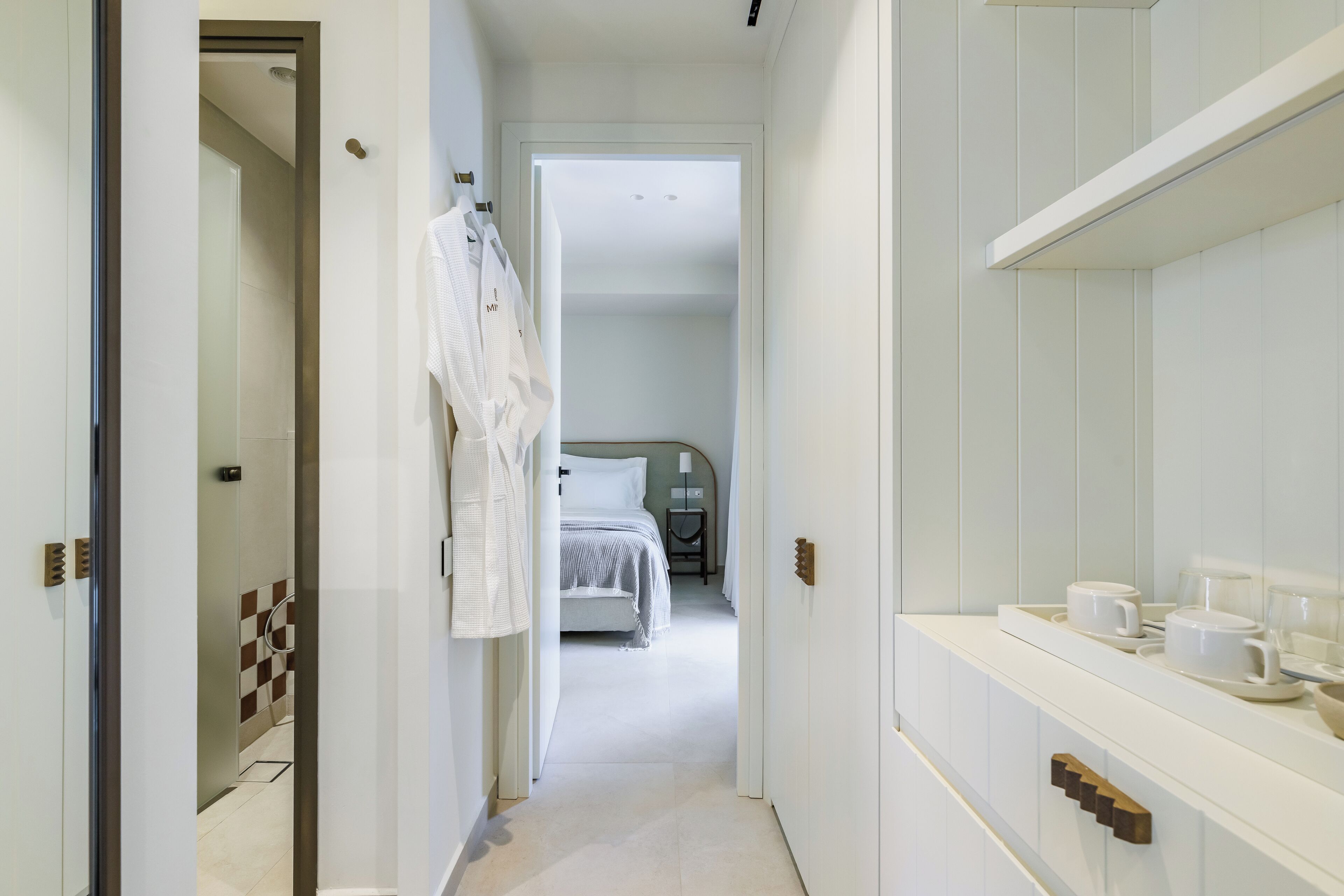 A narrow hallway leading to a bedroom with a bed, a bedside table, and a mirror.