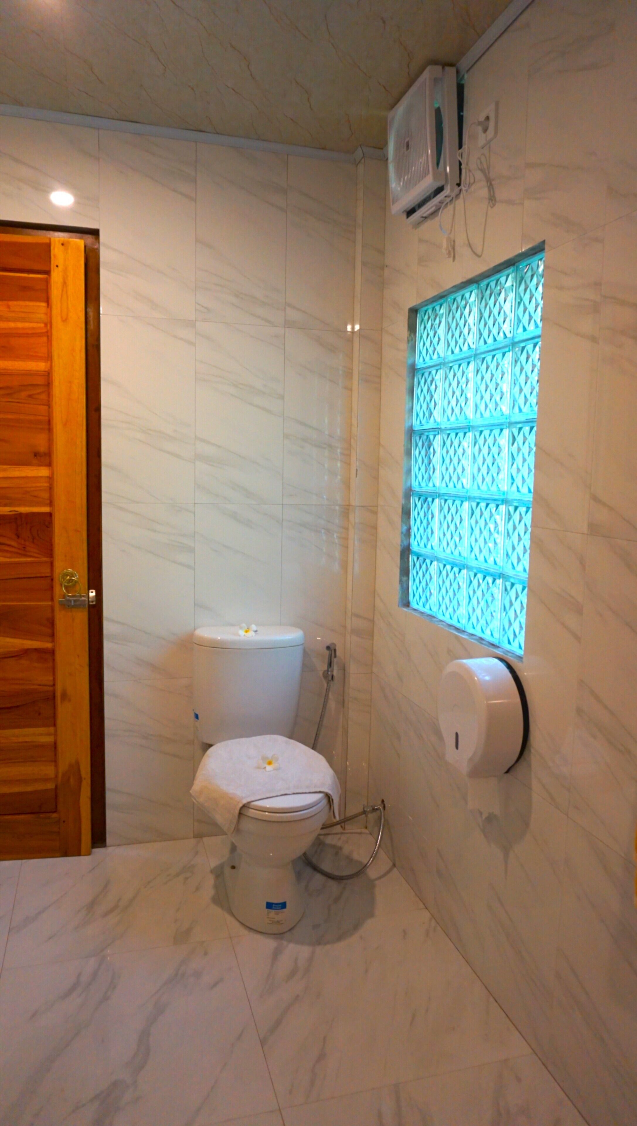 A bathroom with a toilet, a shower, and a window with a blue lattice design.
