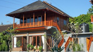 A two-story wooden house with a balcony, a staircase, and a water tank. - Rumah Gajah by Kubukubali (Pemuteran)