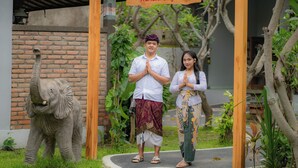 A man and woman in traditional attire standing under a wooden structure with a sign that reads "Rumah Gajah". - Rumah Gajah by Kubukubali (Pemuteran)