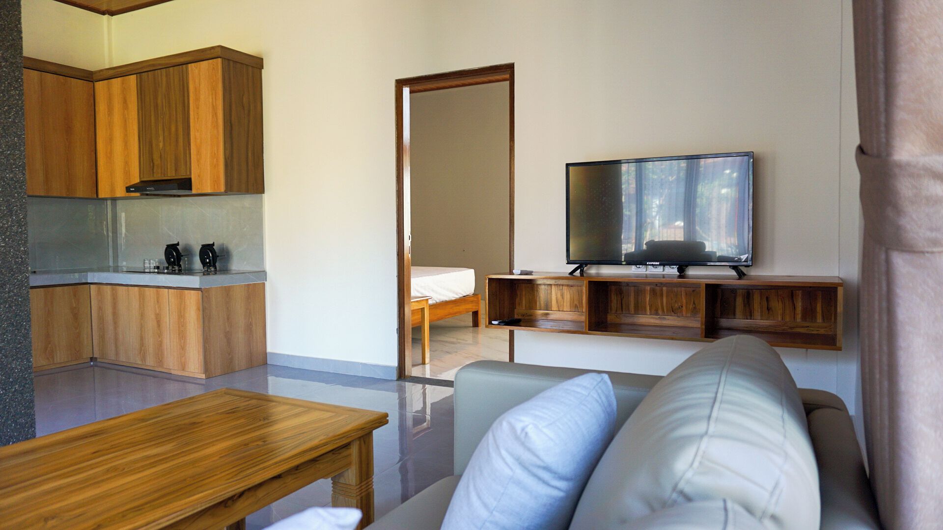 A modern living room with a sofa, a television, wooden cabinets, and a kitchen area.