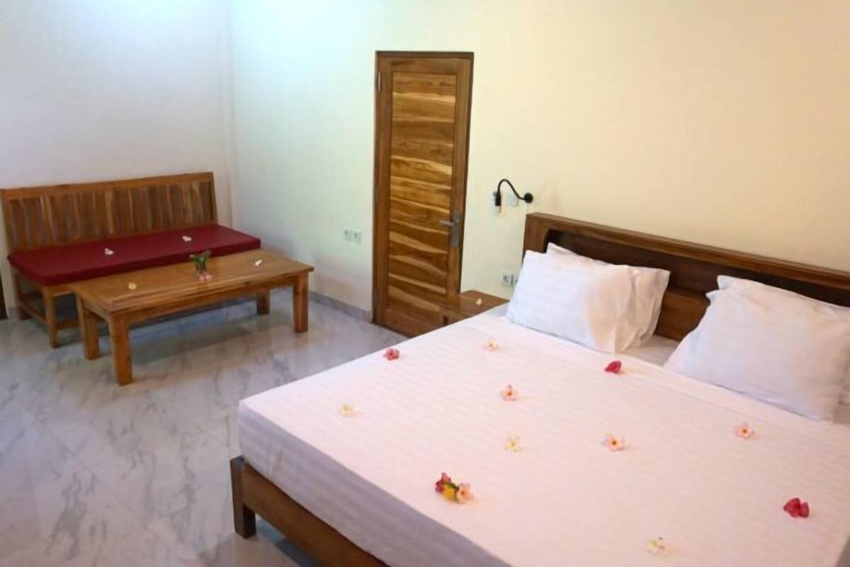 Una habitación de hotel con una cama, un banco de madera, una pequeña mesa y una puerta.