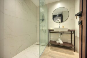 A modern bathroom with a glass-enclosed shower, a round mirror, and a wooden vanity with a sink.