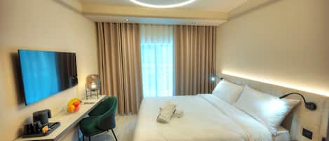 Habitación de hotel con cama, escritorio con silla, televisión de pantalla plana, luz de techo y ventana con cortinas.
