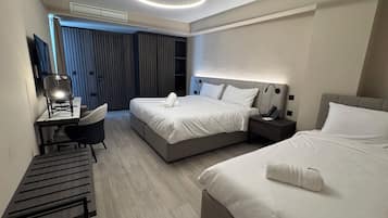 Una habitación de hotel moderna con una cama grande, un escritorio con silla, una mesita de noche con teléfono y un armario con persianas verticales.