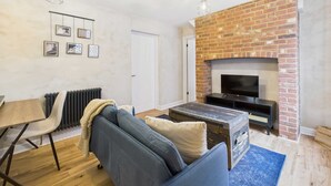 Un salon moderne avec une cheminée en briques, un téléviseur à écran plat, un canapé, une table basse et un coin repas comprenant une table et des chaises.