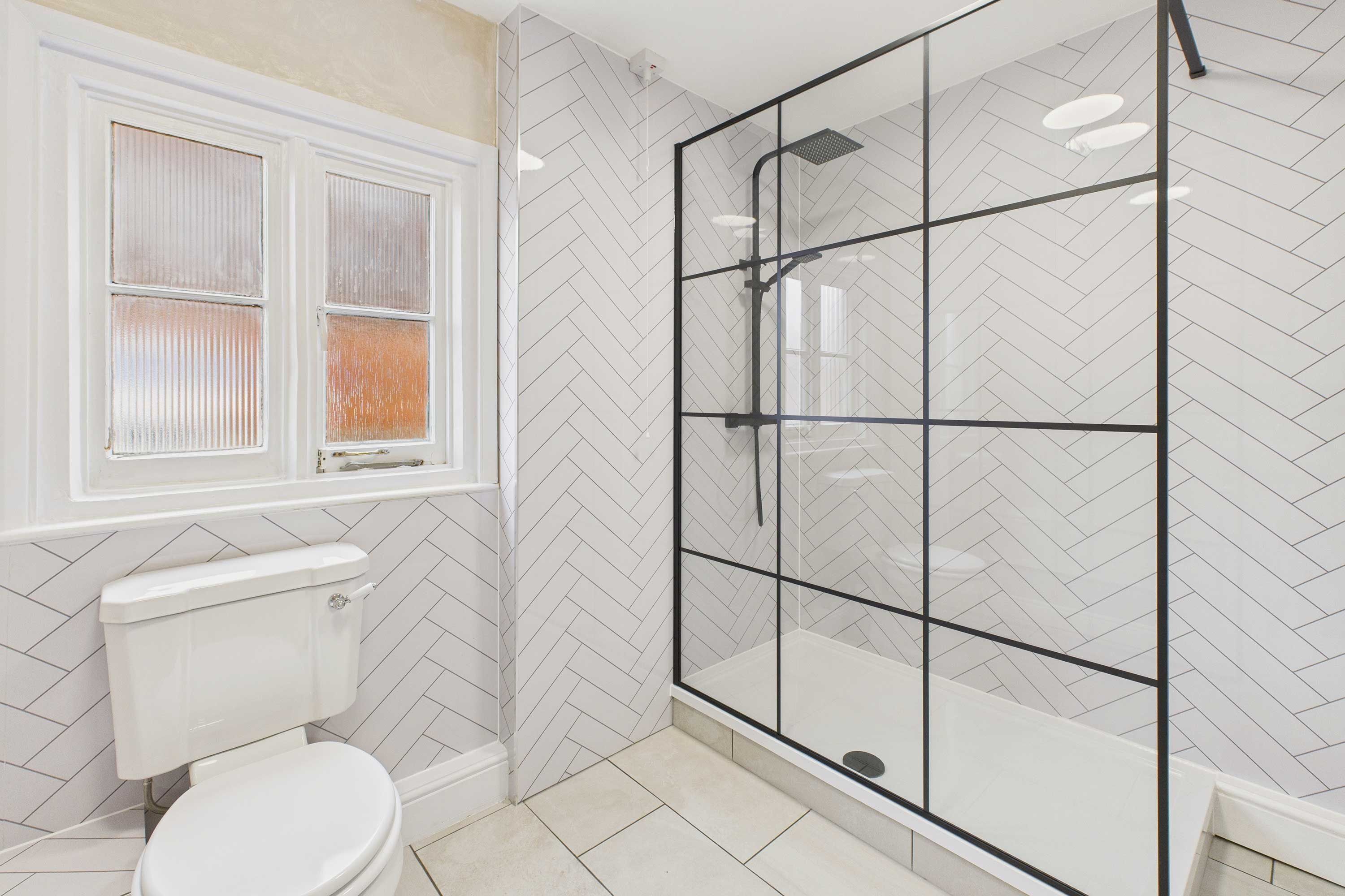 A bathroom with a white toilet, a window with blinds, and a glass shower enclosure.