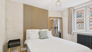Une chambre à coucher comprenant un lit, une table de chevet, un mur avec des lambris en bois, un radiateur et une fenêtre à carreaux.