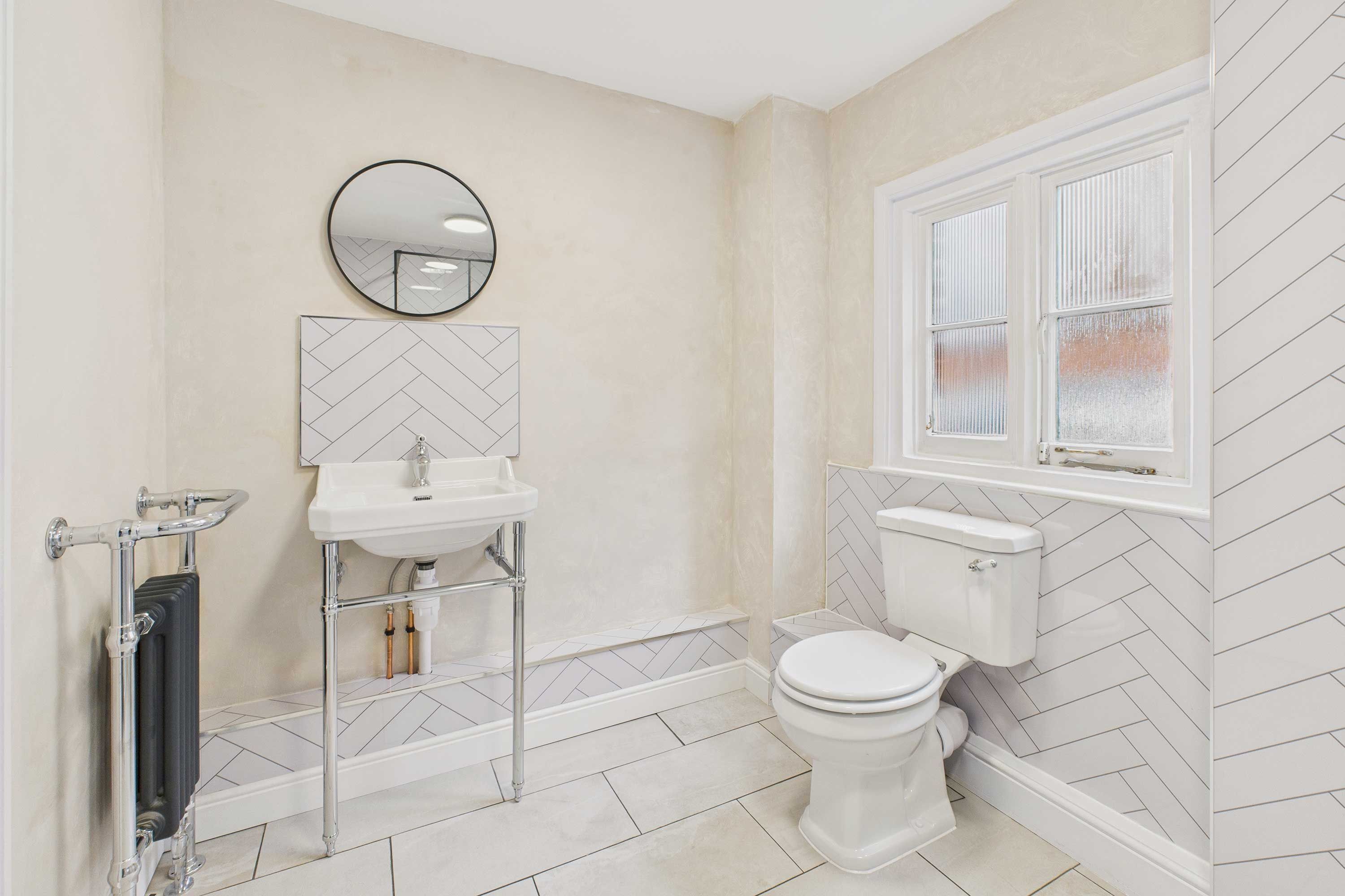 Une salle de bain avec des toilettes blanches, un lavabo, un miroir et un radiateur.