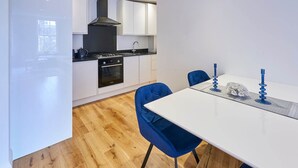 A modern kitchen with white cabinets, a black stove, and a wooden floor. - Host Stay Eton House (Windsor)