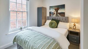 A bedroom with a large bed, a window with a view of a brick wall, a painting of an elephant, and a bedside table with a lamp. - Host Stay Eton House (Windsor)