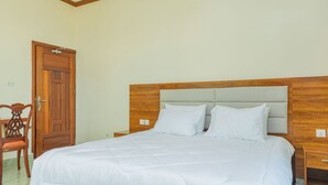 A neatly made bed with a wooden headboard, a wooden nightstand, and a wooden chair with a cushion. - Atlas Residence (Kigali)