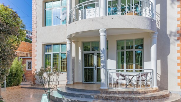 A multi-story building with a balcony, large windows, and a stone pathway leading to the entrance. - Atlas Residence (Kigali)