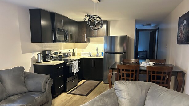A modern kitchen with dark cabinets, a stainless steel refrigerator, and a dining area with a wooden table and chairs.