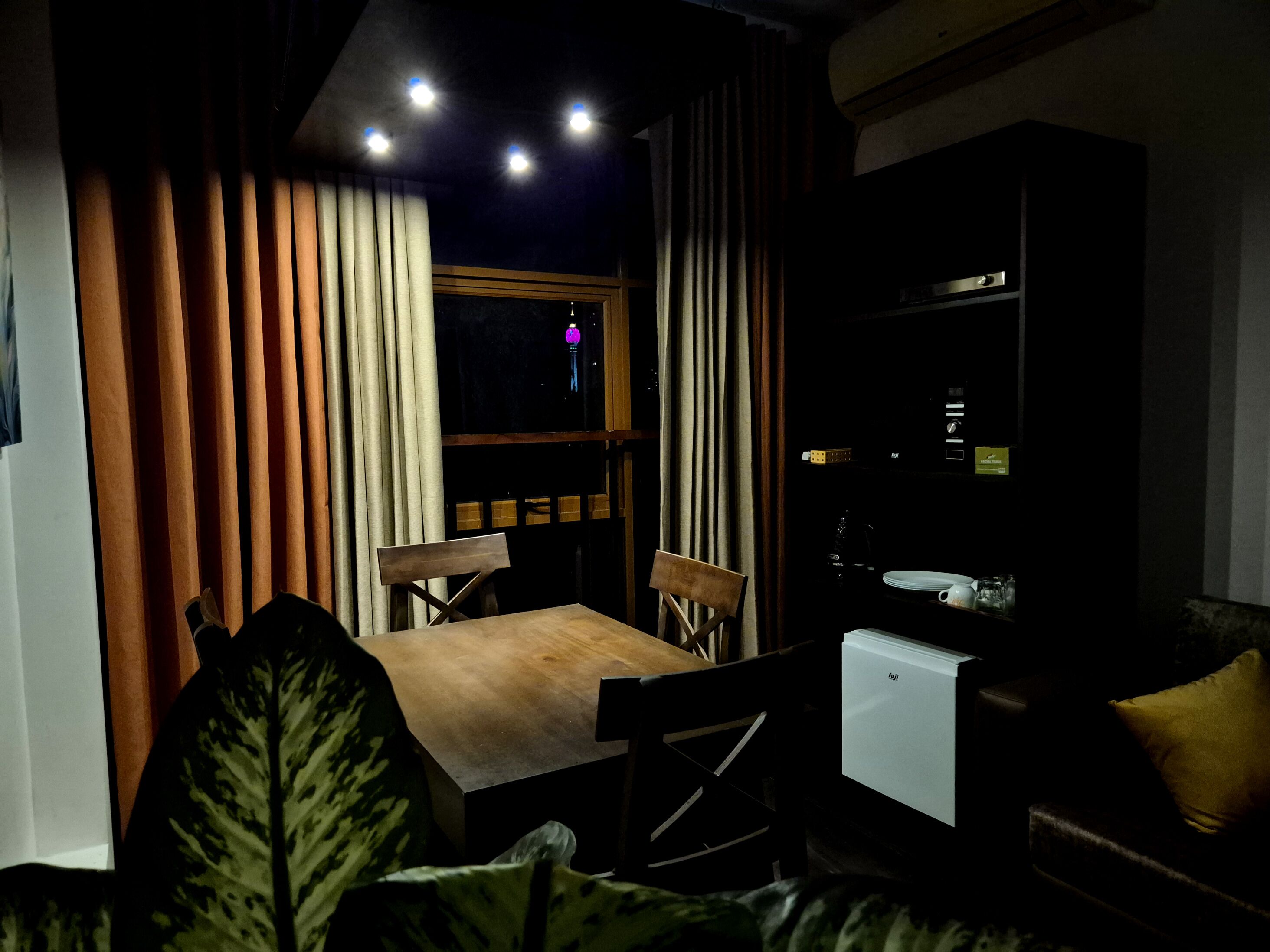 A dimly lit room with a table and chairs, a small white appliance, and a window with curtains.