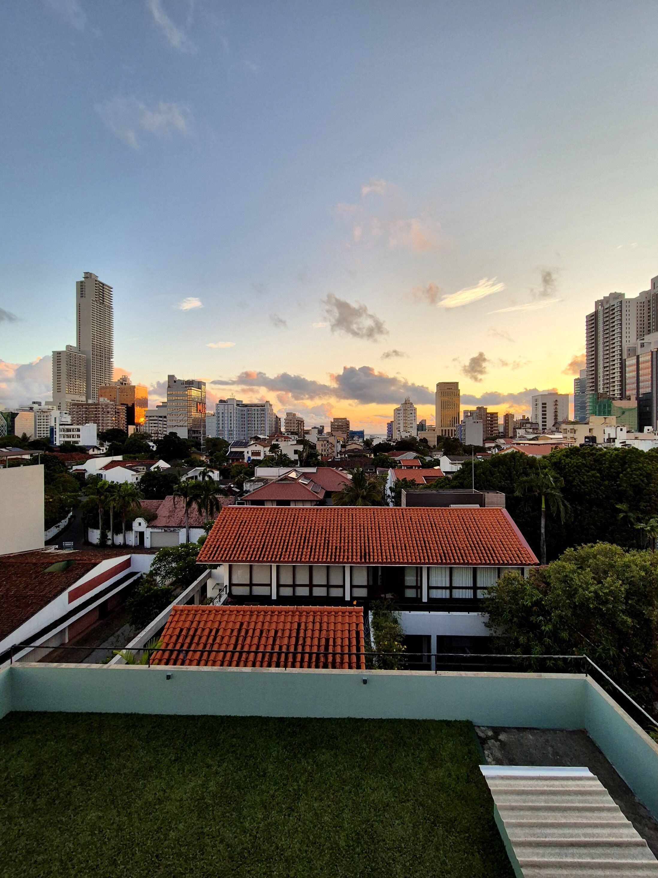A cityscape with a mix of residential and high-rise buildings, a clear sky, and a sunset.