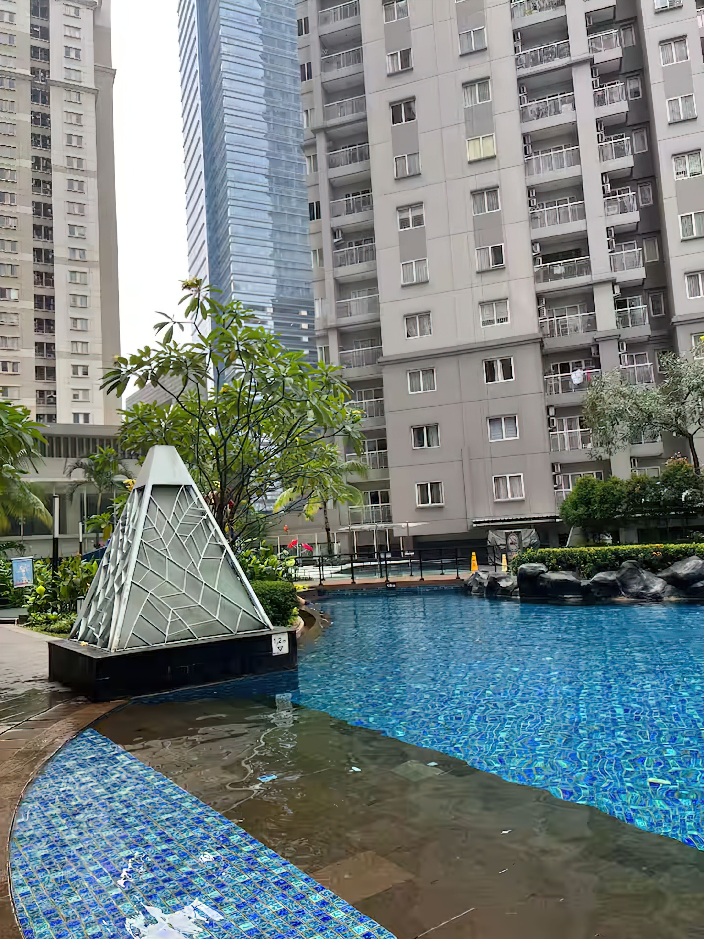 A swimming pool with a glass pyramid structure, surrounded by tall residential buildings.