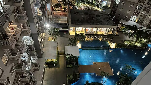 A high-rise building with multiple balconies, a swimming pool with a wooden deck, and a well-lit restaurant area.