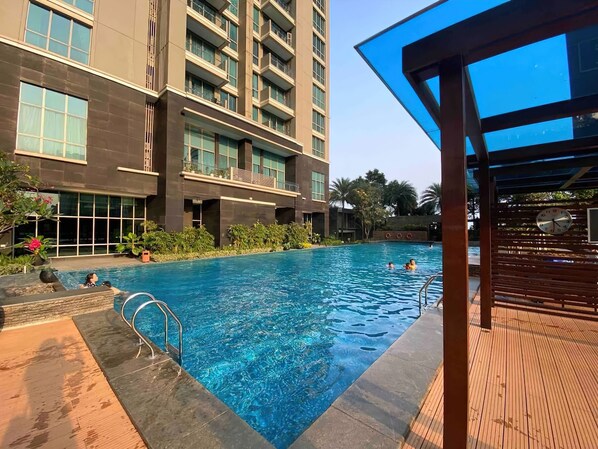 Uma piscina com deck de madeira e um edifício com varandas ao fundo.