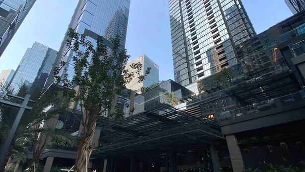 A modern urban area with tall glass buildings, a covered entrance, and a parking area with cars.