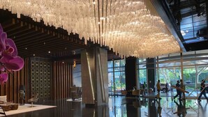 A spacious lobby with a modern chandelier, a seating area, and large windows offering a view of the outdoors.