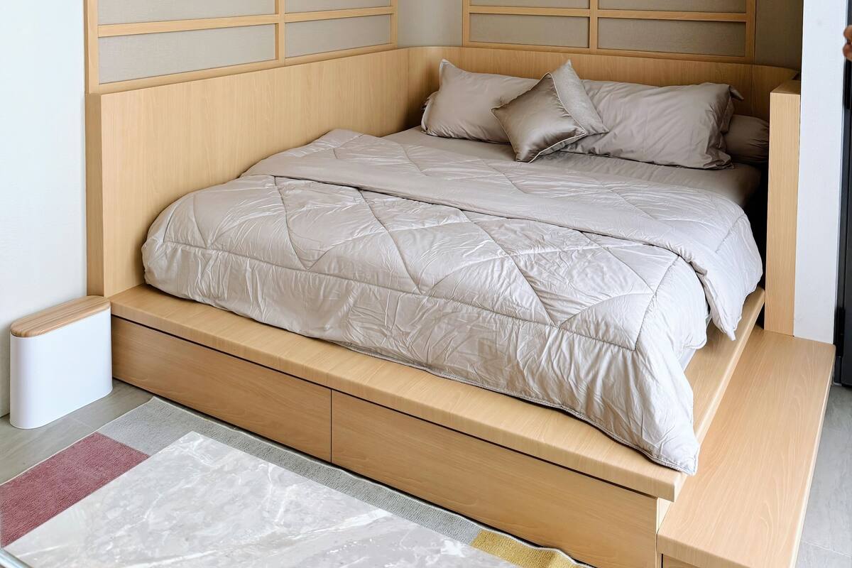 Quarto moderno com cabeceira de madeira, cama com roupa de cama bege e uma pequena mesa de cabeceira.