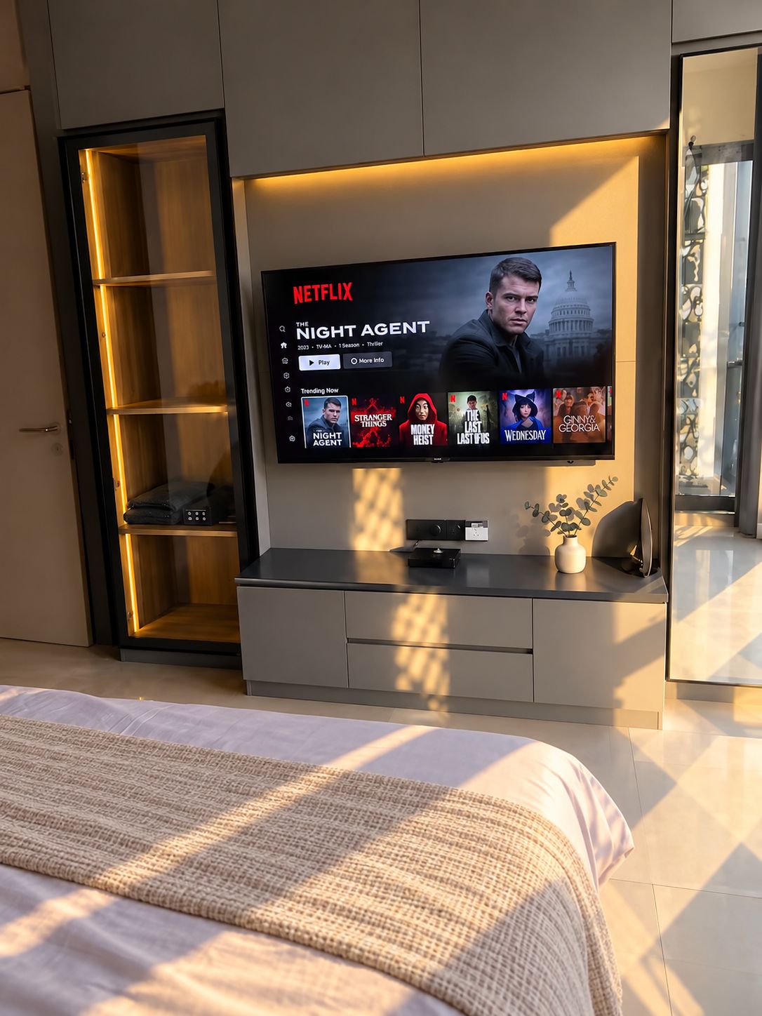 Una sala de estar moderna con un televisor de pantalla plana grande montado en la pared, una estantería empotrada y una cama con una manta texturizada.